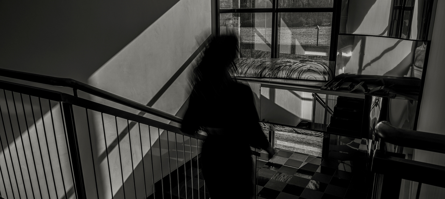 Black and white photo of a person walking downstairs inside the IMTE headquarters, with geometric shadows and industrial reflections creating a modern, sustainable atmosphere.